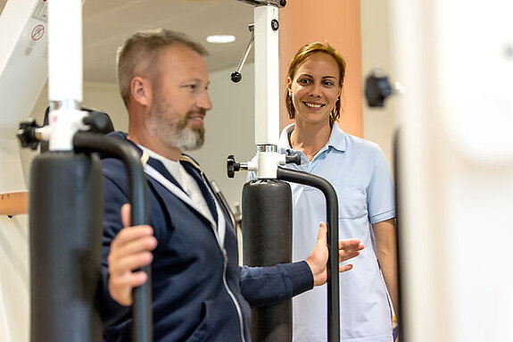 Ein Patient trainiert im Kraftraum in Anwesenheit einer Therapeutin.
