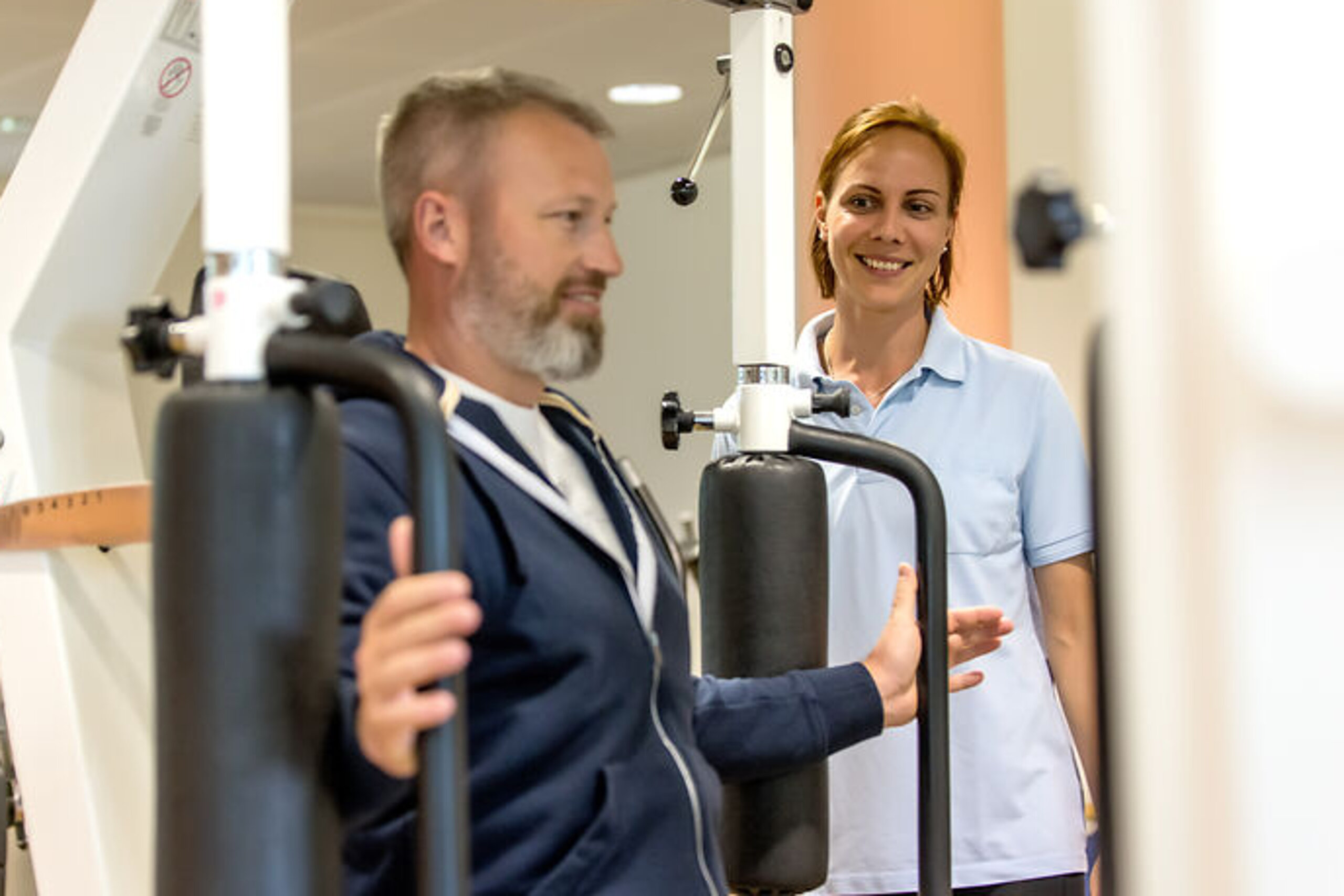 Ein Patient trainiert im Kraftraum in Anwesenheit einer Therapeutin.