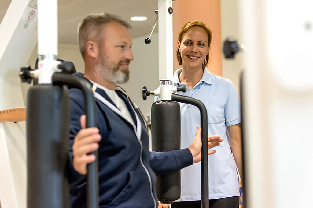 Ein Patient trainiert im Kraftraum in Anwesenheit einer Therapeutin.