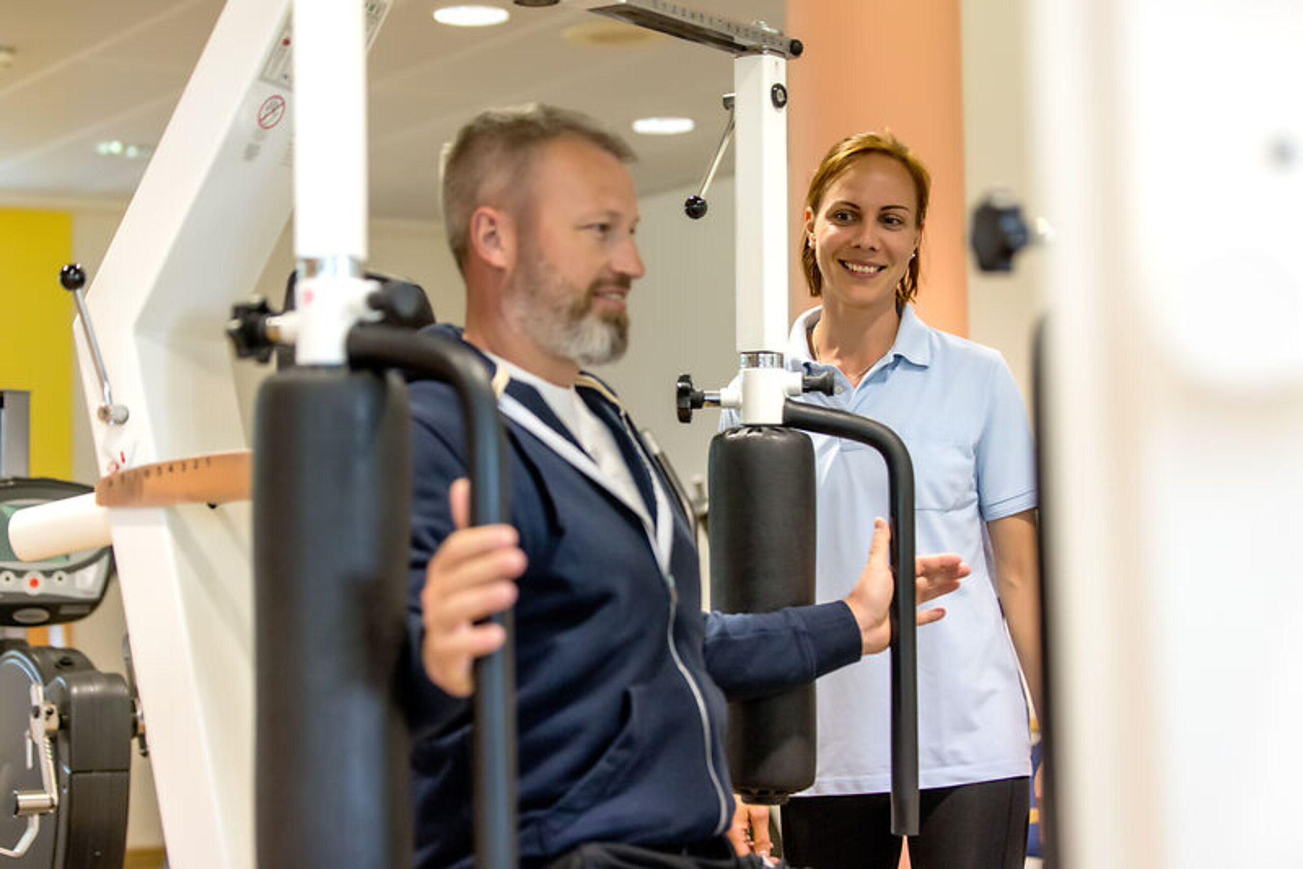 Ein Patient trainiert im Kraftraum in Anwesenheit einer Therapeutin.