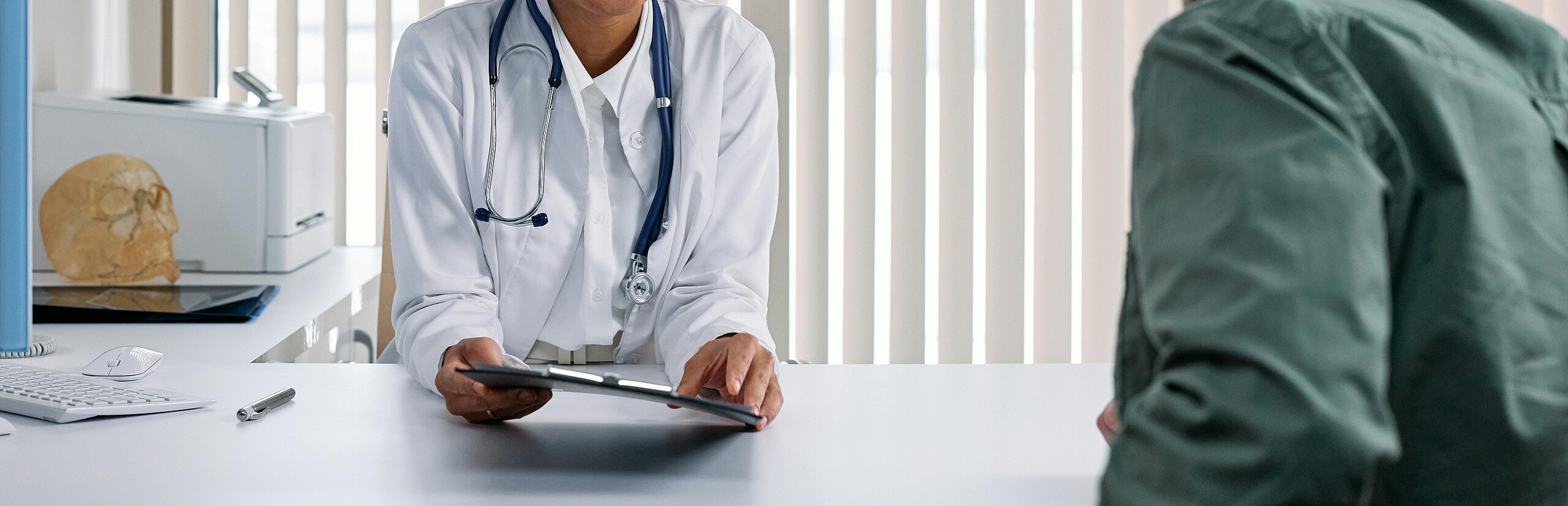 Eine Ärztin im Gespräch mit einem Patienten in einem modernen Praxisraum am Schreibtisch.