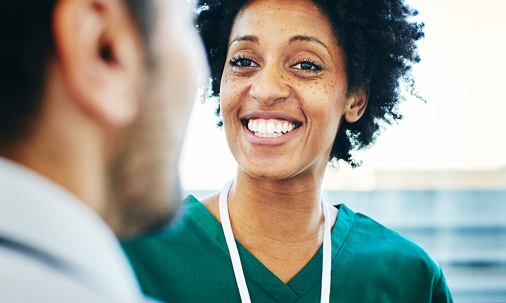 Eine lächelnde Pflegekraft schaut einen Arzt an.