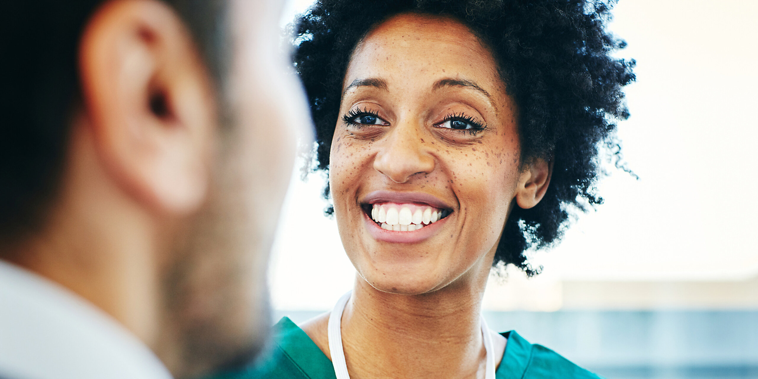 Eine lächelnde Pflegekraft schaut einen Arzt an.