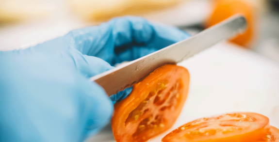 Nahaufnahme vom Schneiden einer Tomate mit einem Messer.