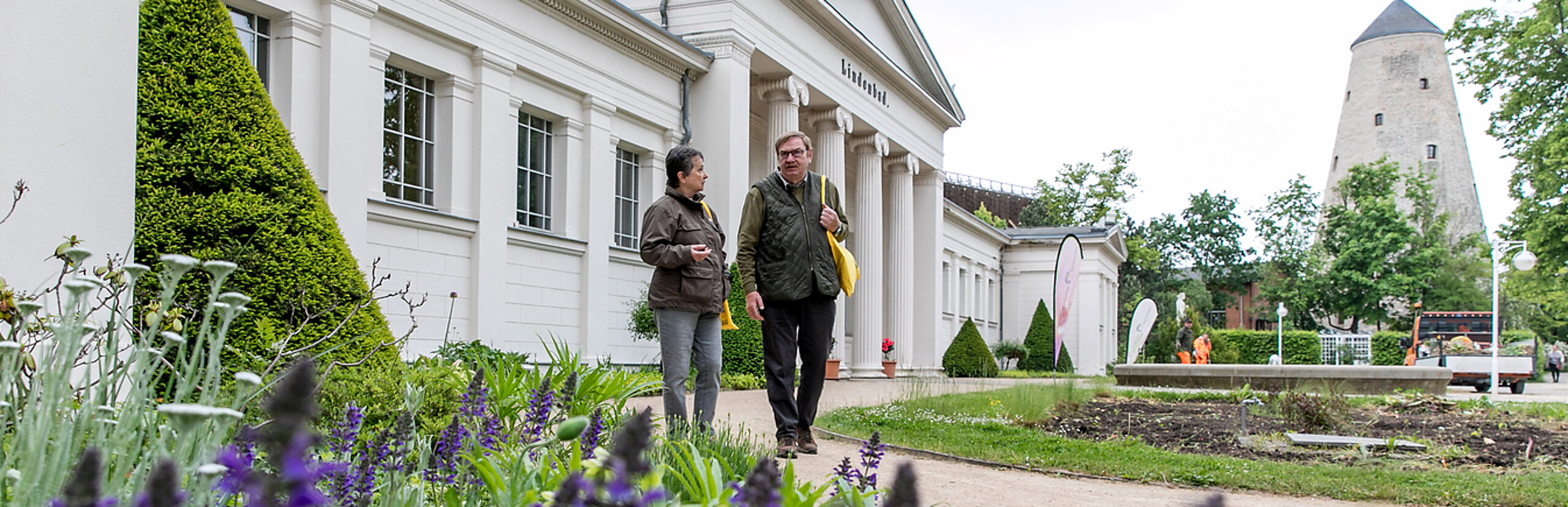 Zwei Personen laufen durch den Kurpark, hinter ihnen befindet sich das Lindenbad und der Soleturm.
