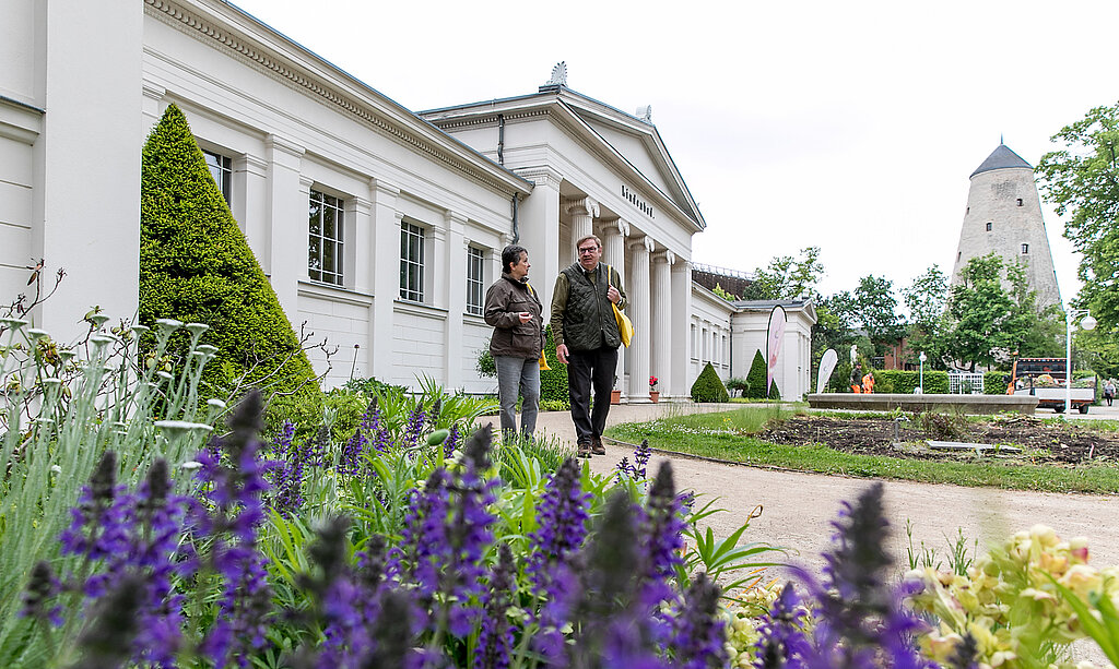 Zwei Personen laufen durch den Kurpark, hinter ihnen befindet sich das Lindenbad und der Soleturm.