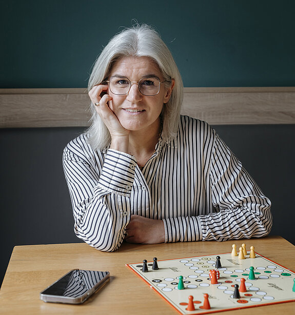Nora Volmer-Berthele sitzt mit einem Spiel am Tisch.