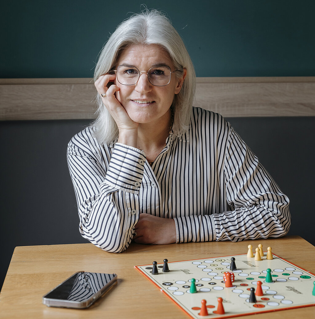 Nora Volmer-Berthele sitzt mit einem Spiel am Tisch.
