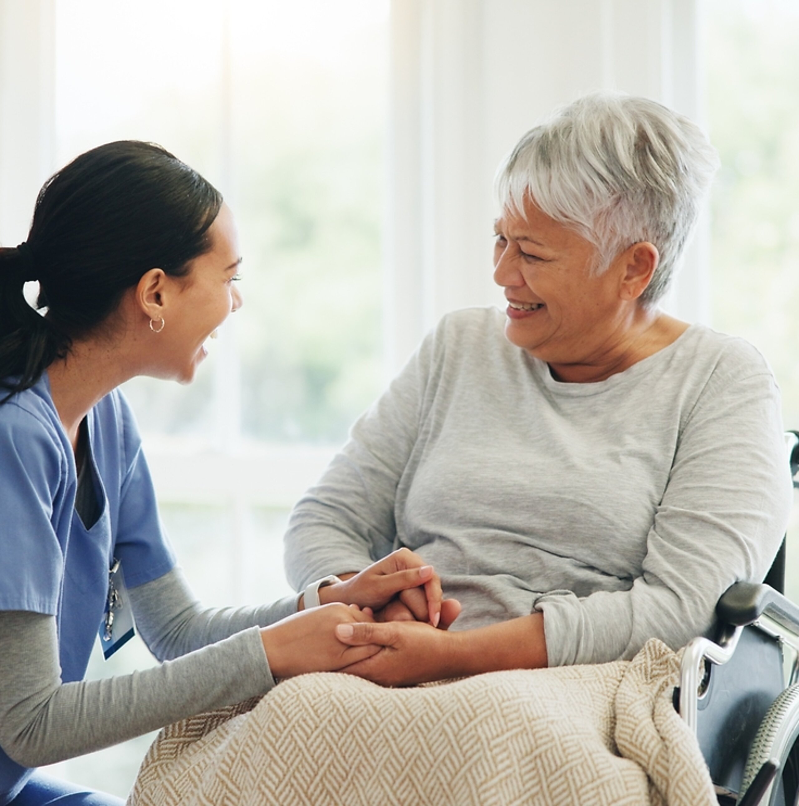 Pflegerin mit Patientin Eine Pflegerin hält vertrauensvoll die Hand einer Patientin im Rollstuhl.