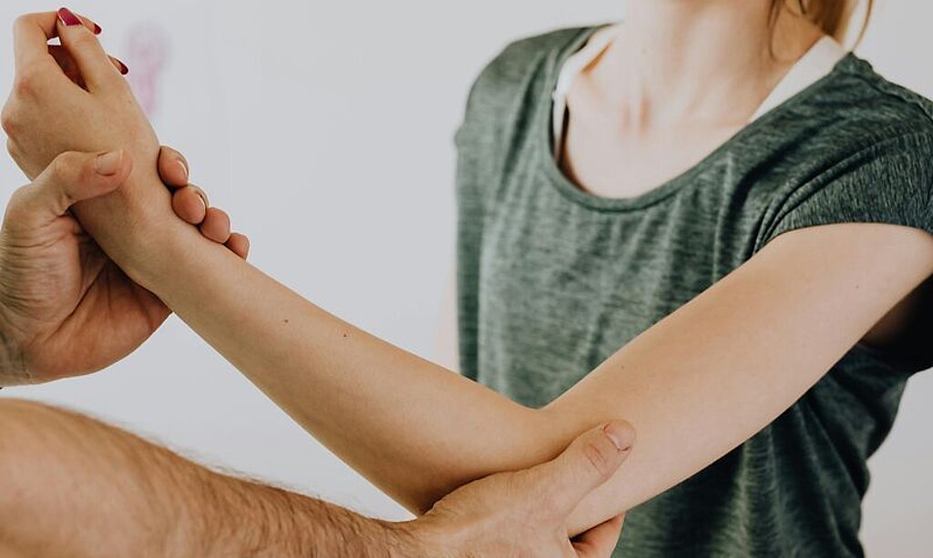 Ein Therapeut behandelt den Ellenbogen einer Patientin.