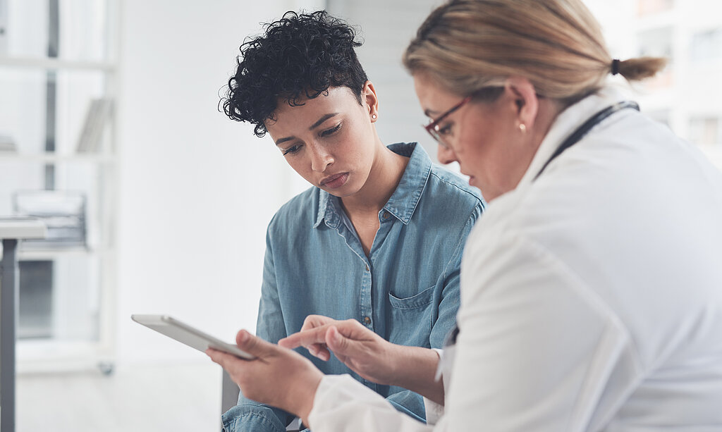 Eine Ärztin zeigt einer jungen Patientin etwas an einem Tablet.