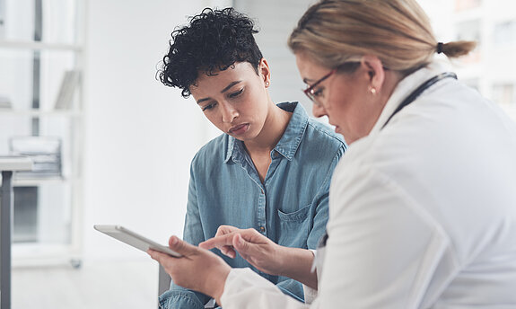 Eine Ärztin zeigt einer jungen Patientin etwas an einem Tablet.