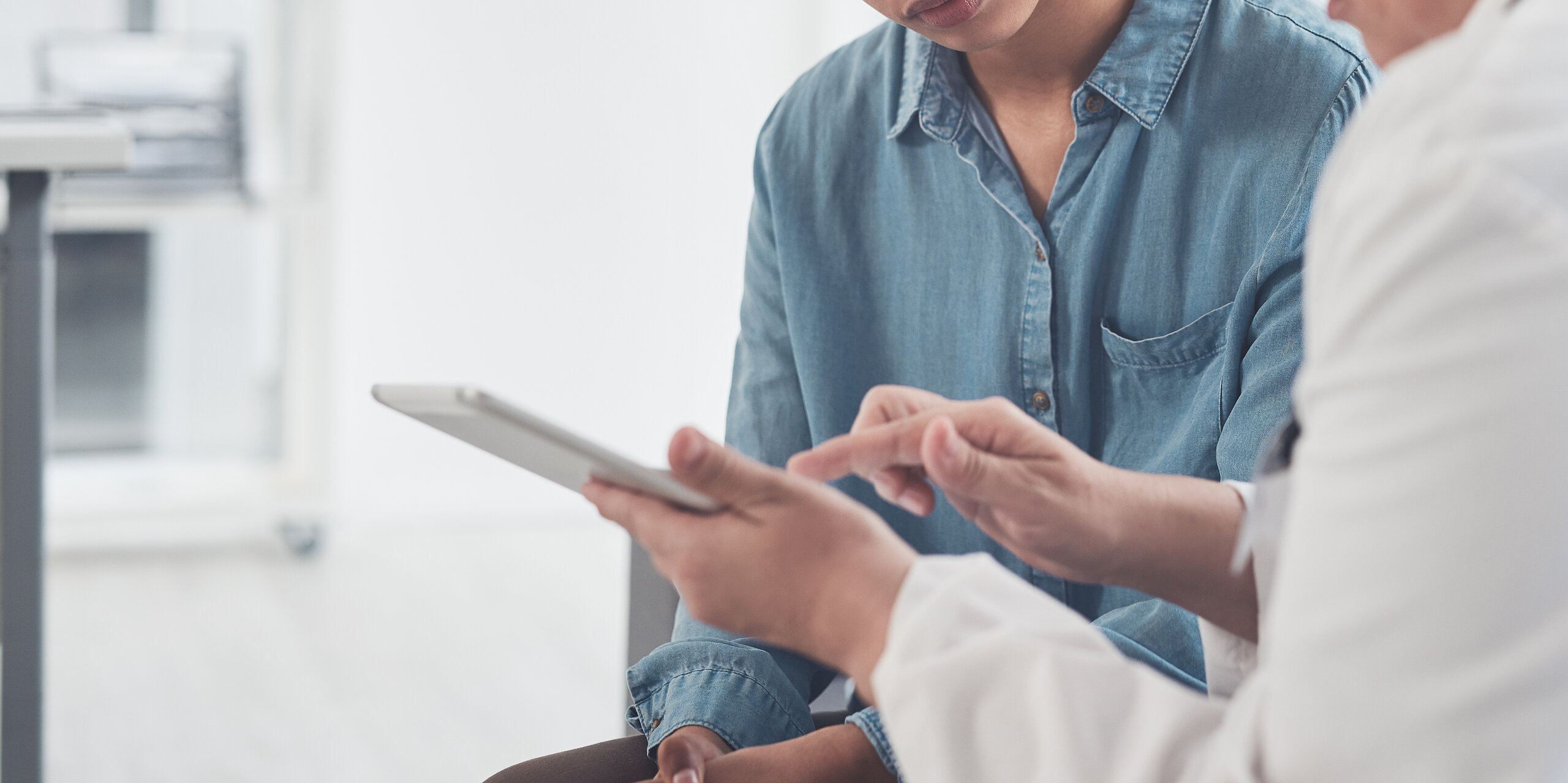 Eine Ärztin zeigt einer jungen Patientin etwas an einem Tablet.