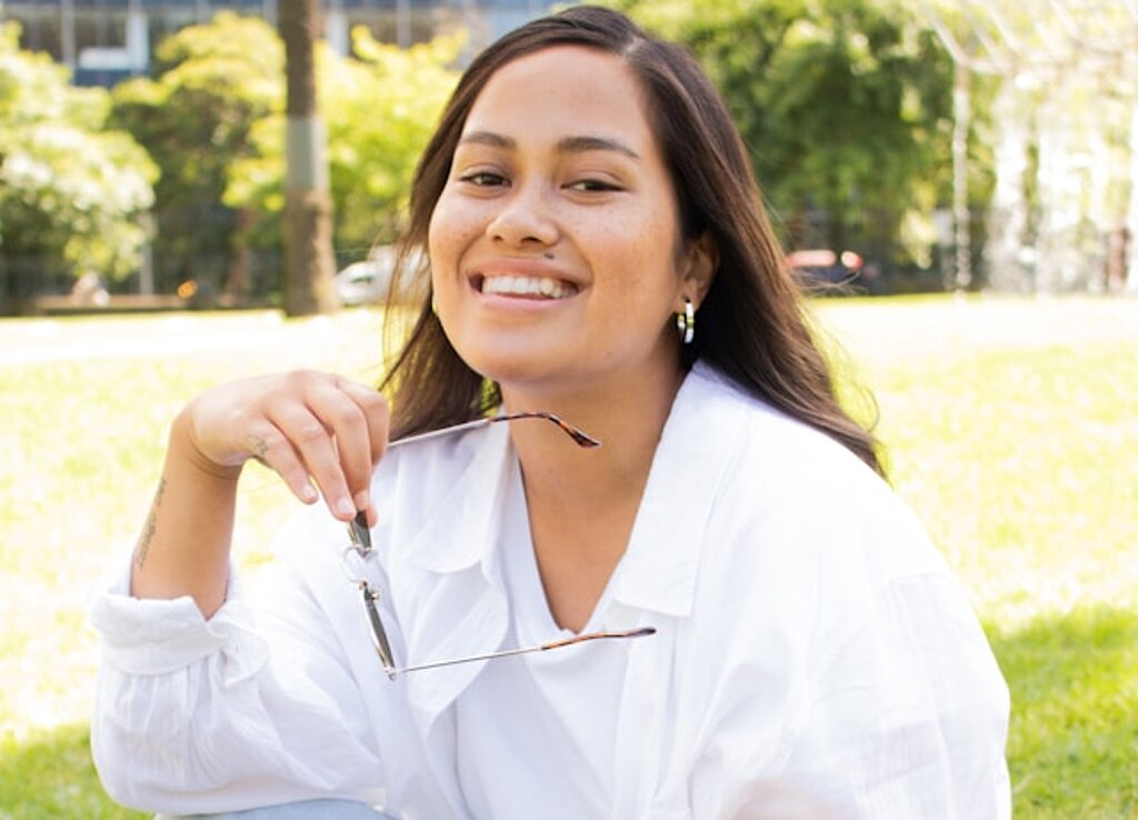 Studentin Park Eine Studentin sitzt lachend im Park mit Tasche.