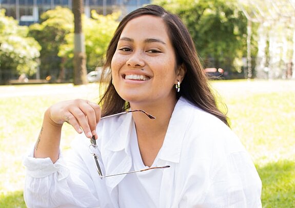 Studentin Park Eine Studentin sitzt lachend im Park mit Tasche.