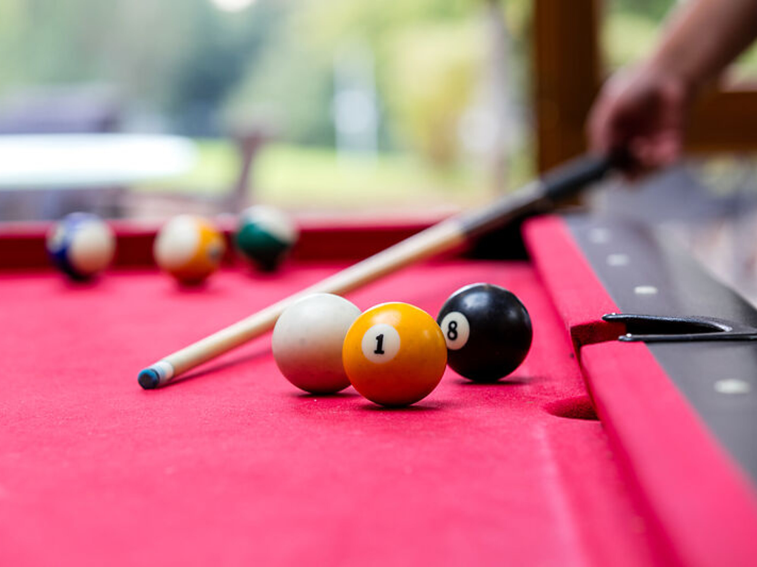 Das Bild zeigt einen Ausschnitt eines Billard-Tisches mit Kugeln, eine Hand hält einen Billardqueue.