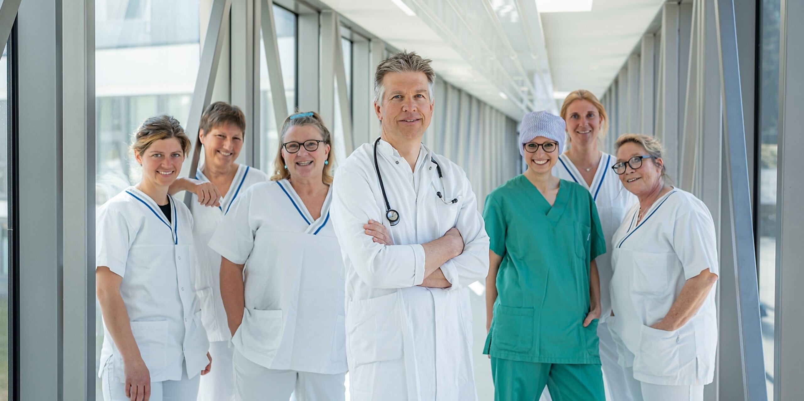Ein Team aus Arzt und mehreren Pflegekräften steht in einem Glasgang.