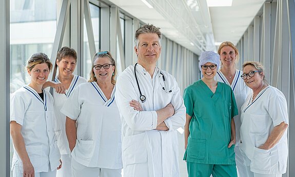 Ein Team aus Arzt und mehreren Pflegekräften steht in einem Glasgang.