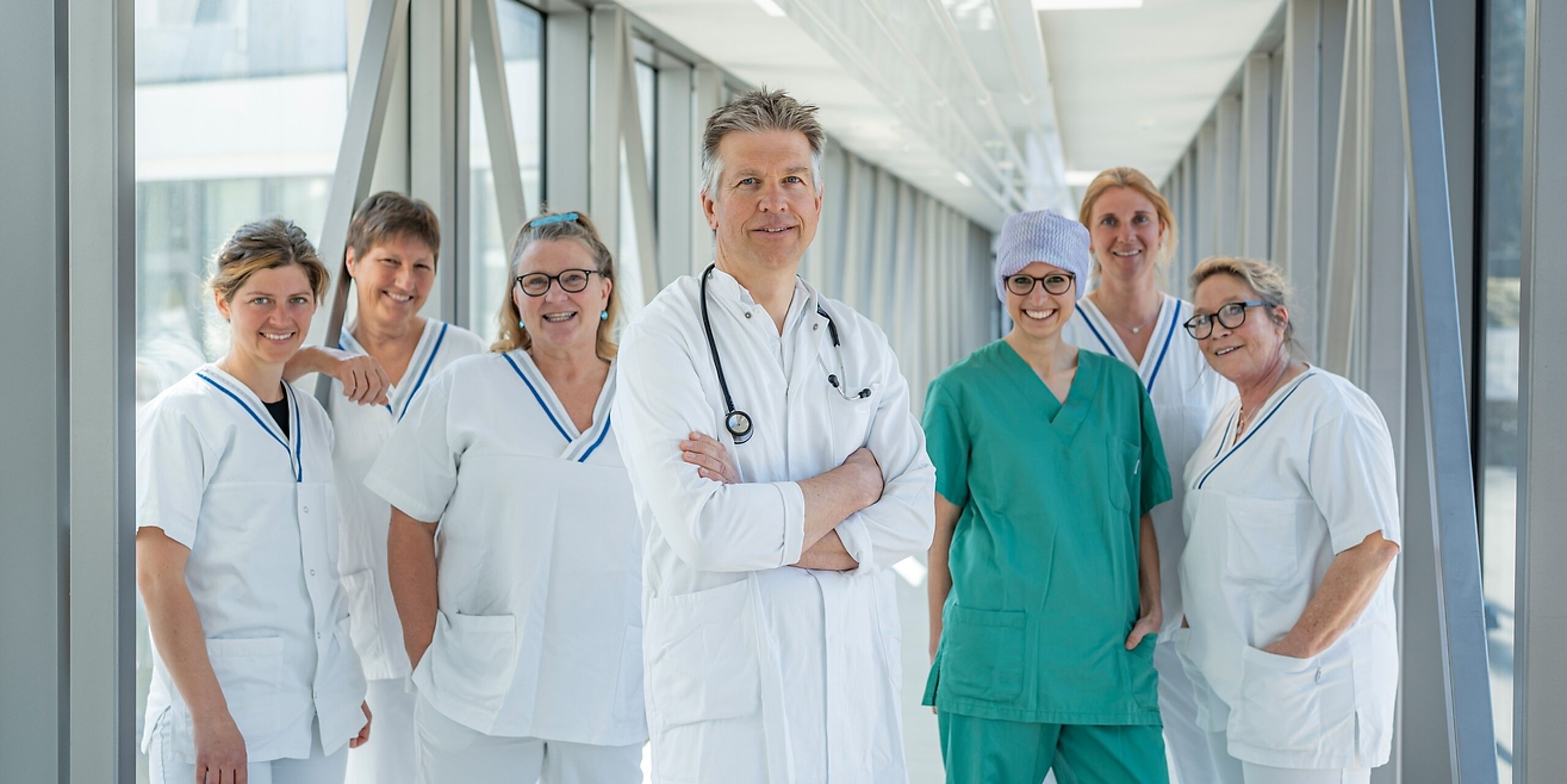 Ein Team aus Arzt und mehreren Pflegekräften steht in einem Glasgang.