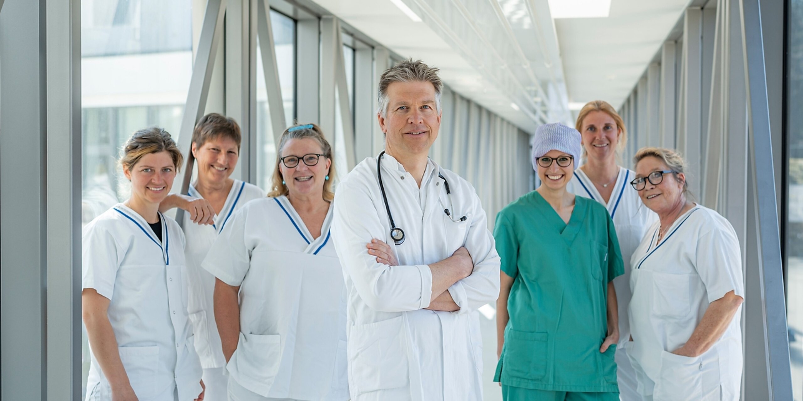 Ein Team aus Arzt und mehreren Pflegekräften steht in einem Glasgang.